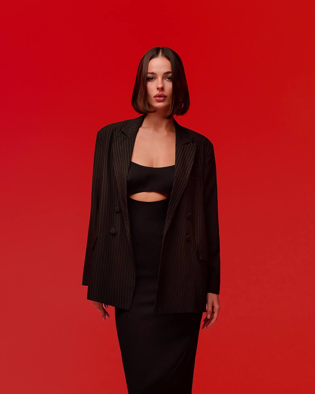 Woman wearing a black pinstripe blazer over a black top and skirt on a red background