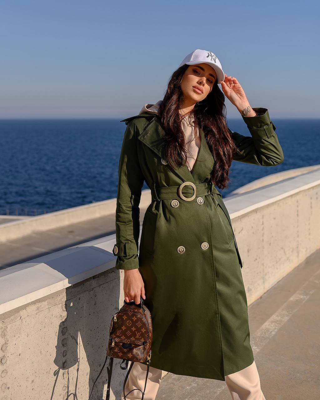 Woman in a green trench coat standing by the ocean