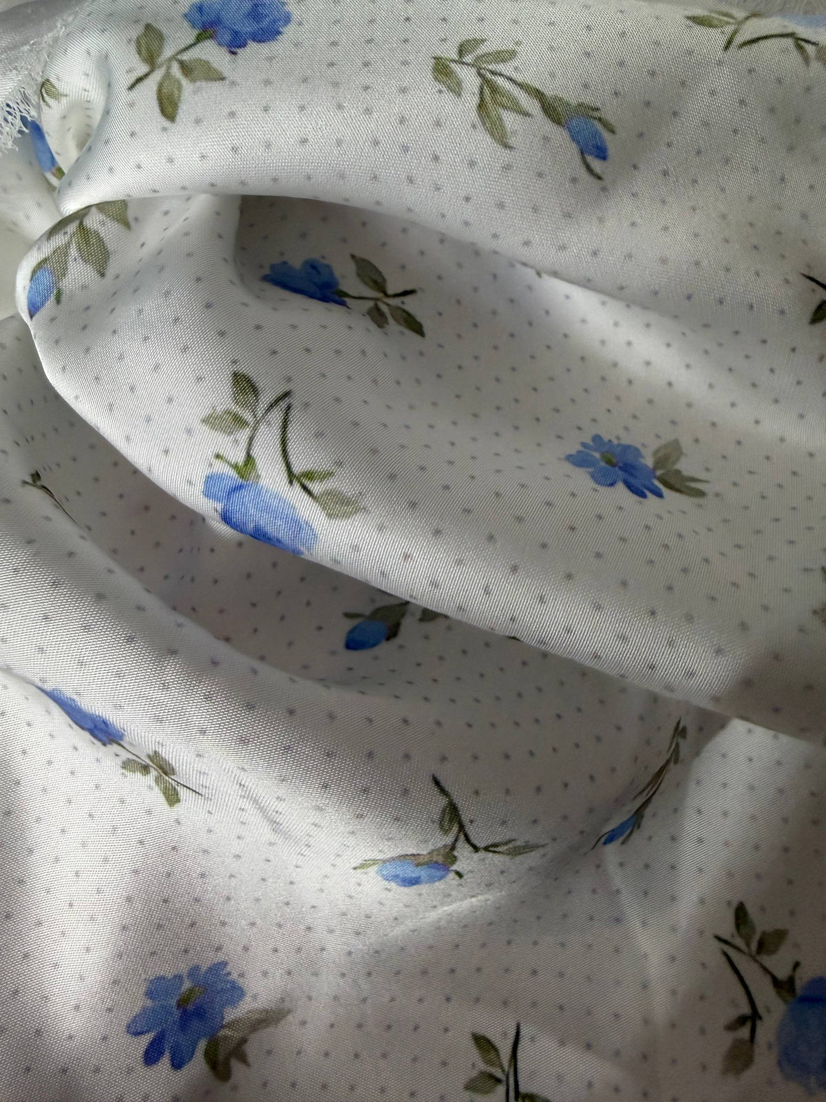 Floral patterned fabric with blue flowers and green leaves on a white background