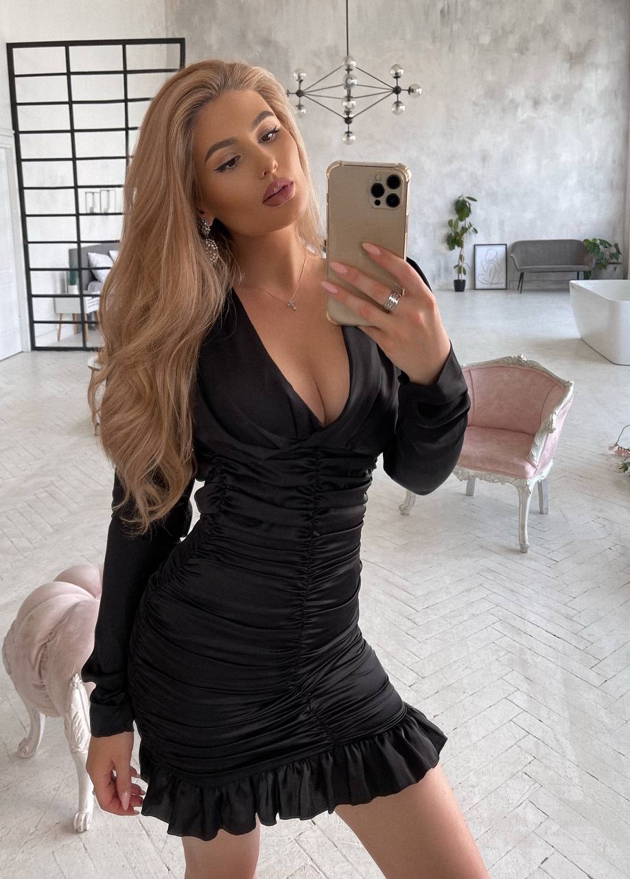 Woman taking a mirror selfie in a black dress in a modern living room.