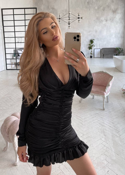 Woman taking a mirror selfie in a black dress in a modern living room.