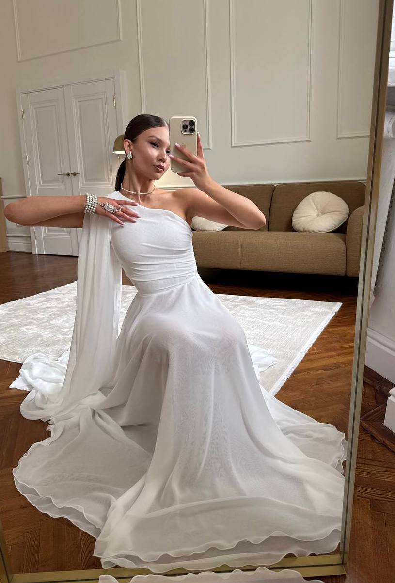 Woman in a white wedding dress taking a mirror selfie in a room with a couch and rug.