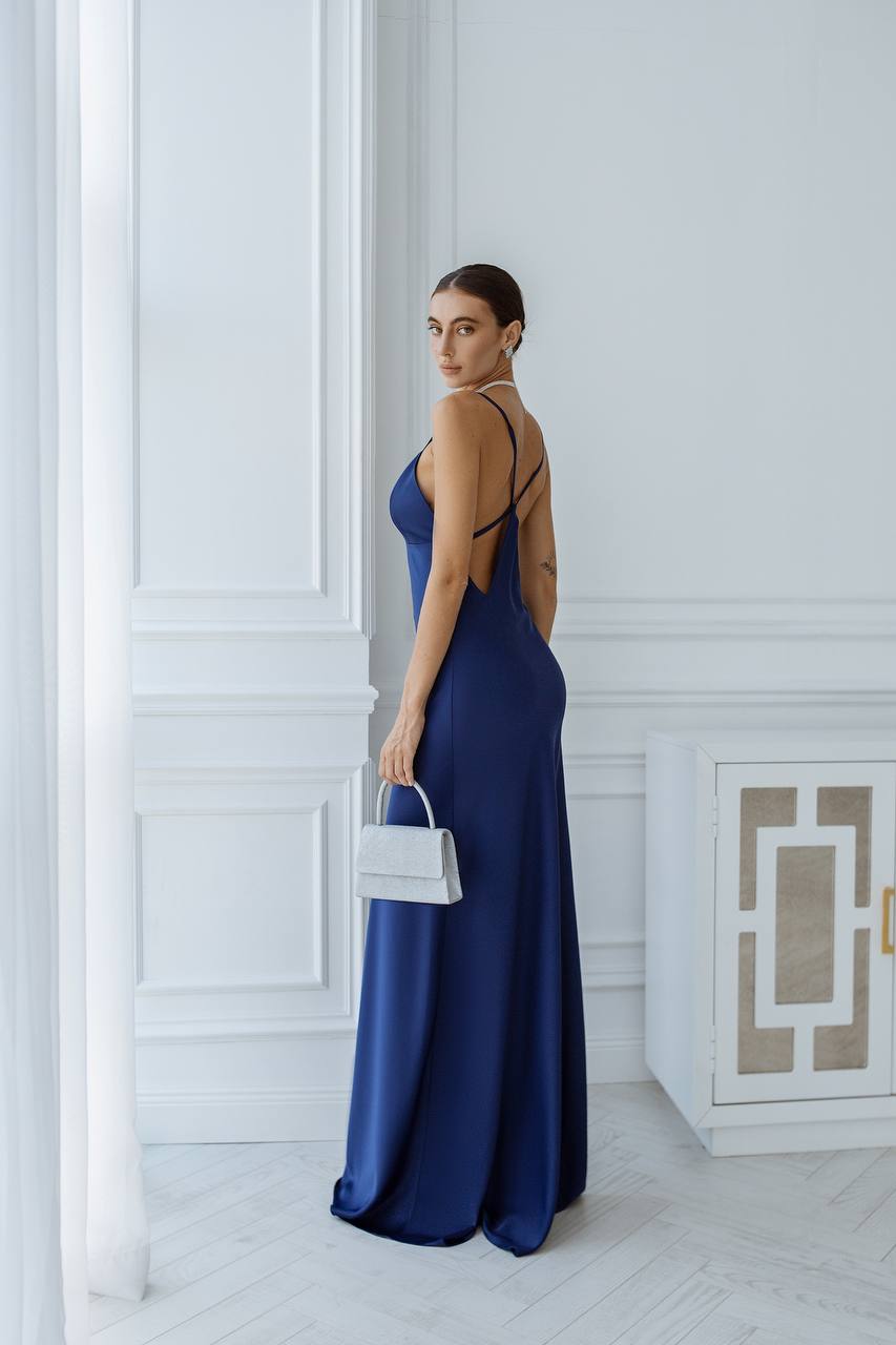 Woman in a blue evening gown standing in a room with white walls and a cabinet.