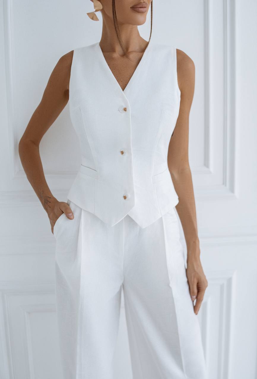 Woman wearing a white sleeveless top and pants against a white background
