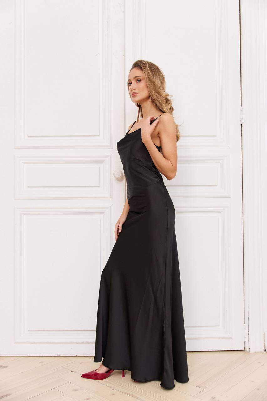 Woman wearing a black evening gown against a white paneled wall.