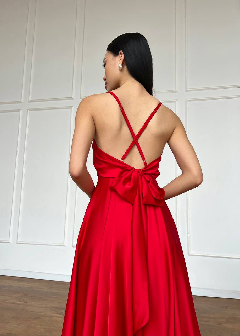 Woman wearing a red dress with a bow detail on a white paneled wall.