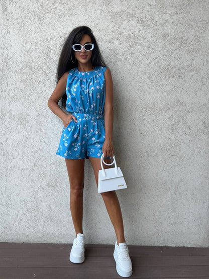 Woman wearing a blue floral dress with white sneakers against a gray wall.