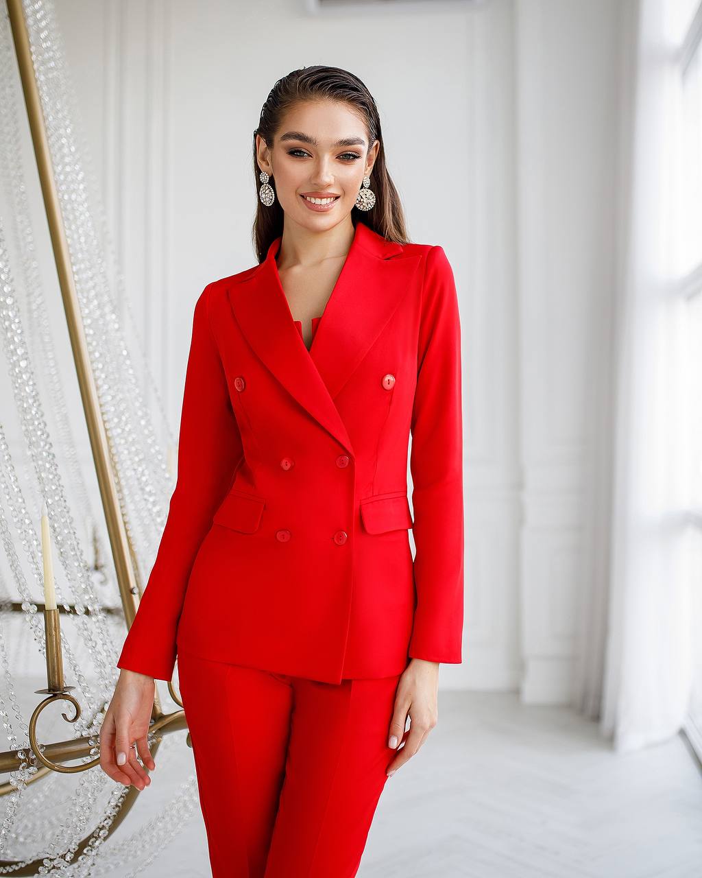 Woman wearing a red suit in a bright room with decorative elements.