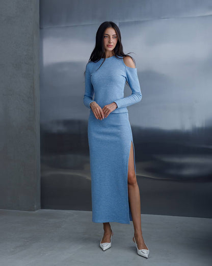 Woman wearing a blue dress with a slit standing against a gray background
