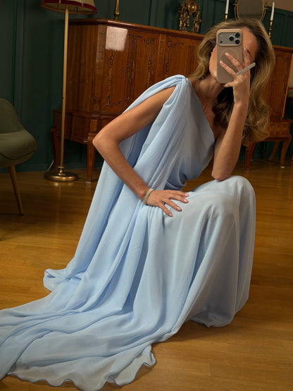 Woman in a light blue dress sitting on the floor in a room with wooden floors and furniture.