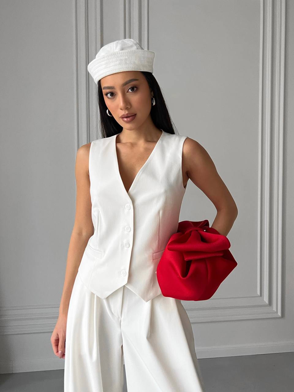 Woman in white outfit holding a red clutch against a gray wall