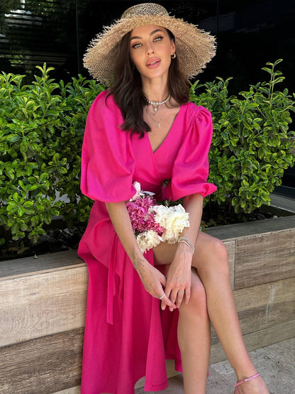 Woman in a bright pink dress and straw hat holding flowers, sitting outdoors.
