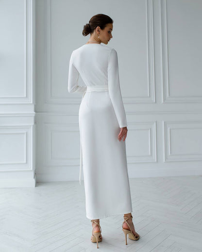 Woman wearing a white long-sleeve dress in a minimalistic room.