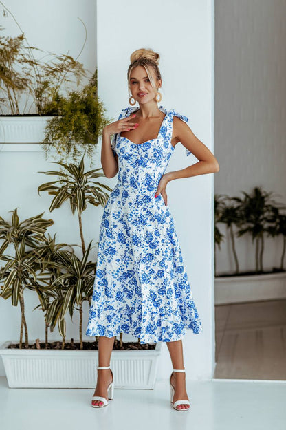 Woman wearing a blue floral dress standing in front of plants.