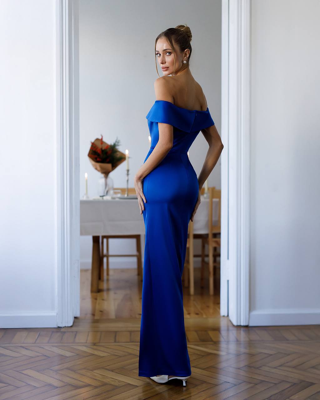 Woman in a blue off-shoulder gown standing in a room with wooden flooring.