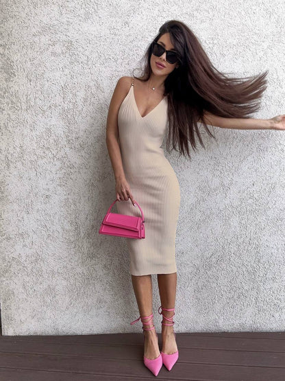 Woman in a beige dress with a pink handbag against a textured wall.
