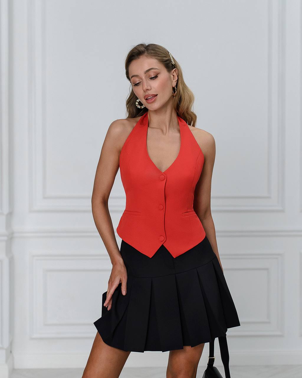 Woman wearing a red top and black skirt against a white paneled wall.