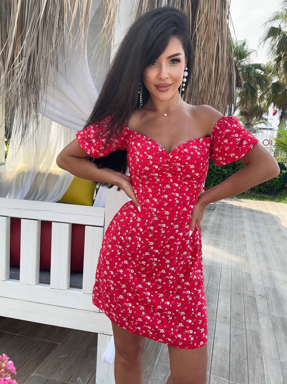 Woman wearing a red floral dress standing outdoors with palm trees in the background