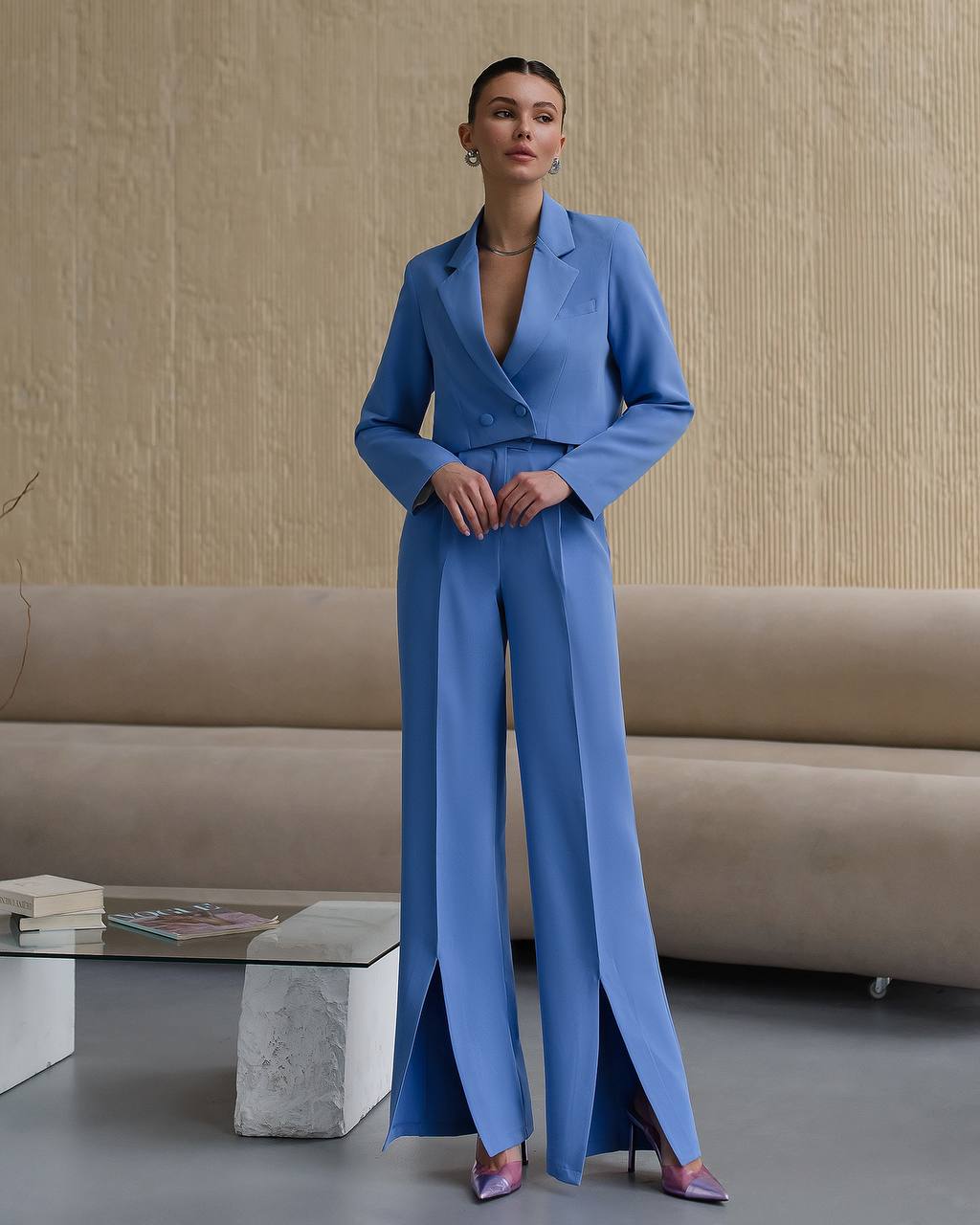 Woman in a blue suit standing in a room with a beige sofa and coffee table.