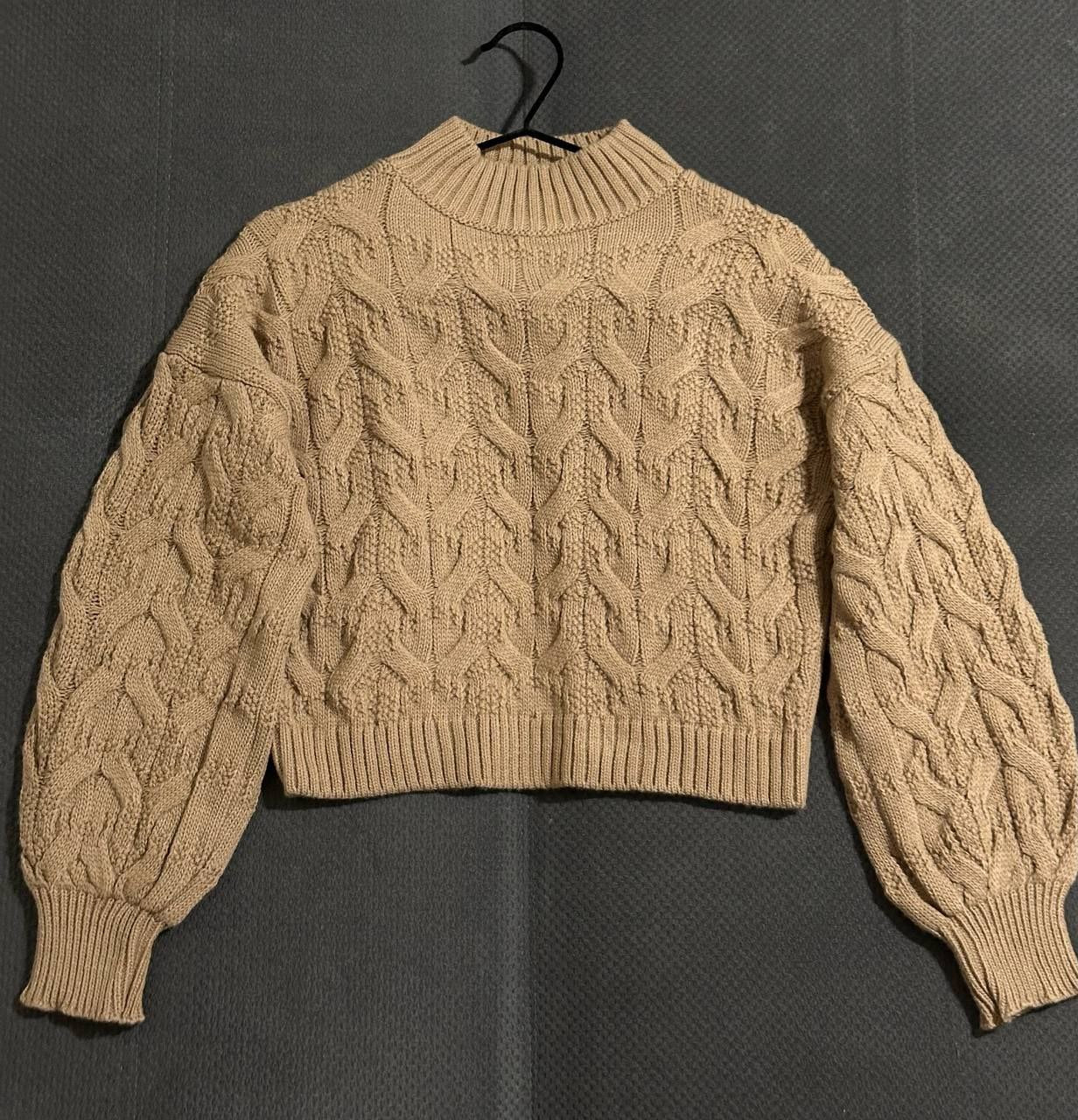 Beige cable knit sweater on a dark background