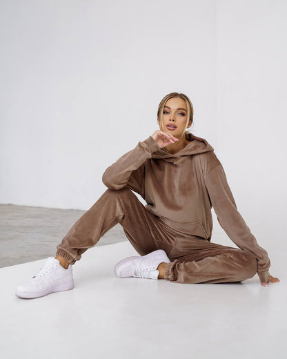Woman wearing a brown tracksuit sitting on a white floor with a white background