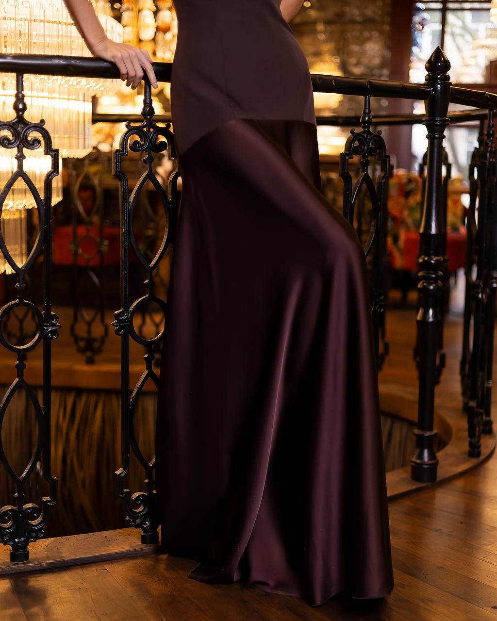 Person wearing a long, dark purple dress standing behind an ornate black railing.