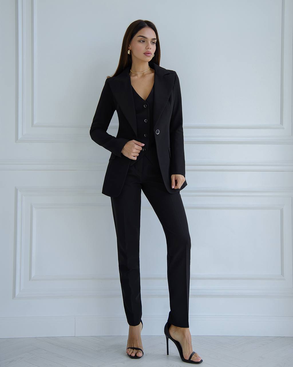 Woman wearing a black suit standing against a white paneled wall.