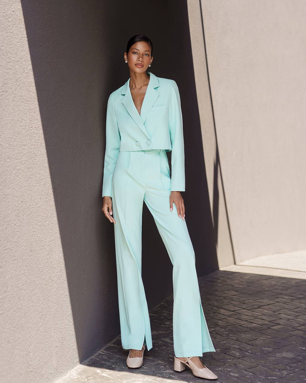 Woman wearing a light blue suit standing against a neutral wall.