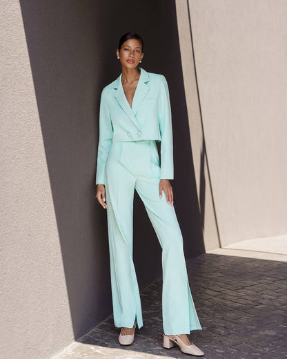 Woman wearing a light blue suit standing against a neutral wall.