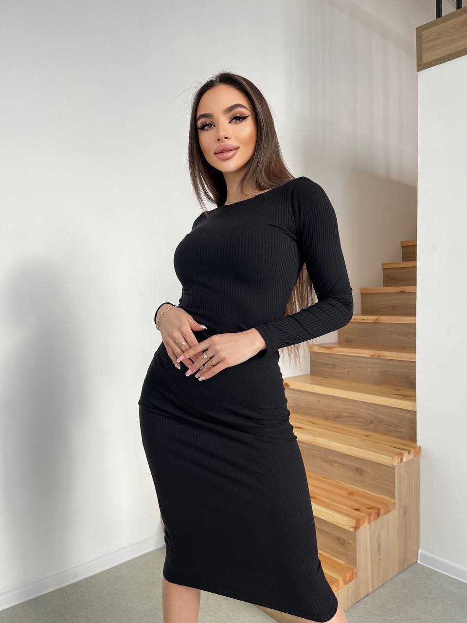 Woman wearing a black dress standing in a modern interior setting with wooden stairs.