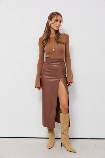 Woman wearing a brown long-sleeve top and leather skirt with beige high-heeled boots against a white background