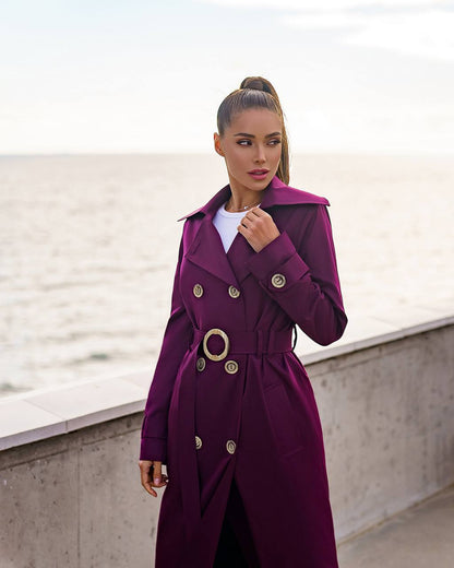Woman wearing a purple trench coat with gold buttons against a light background