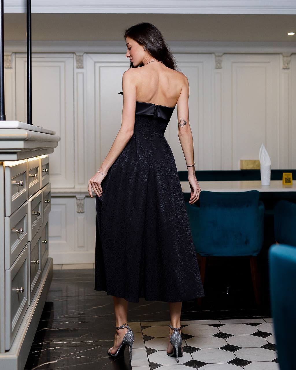 Woman in a black dress standing in a modern kitchen.