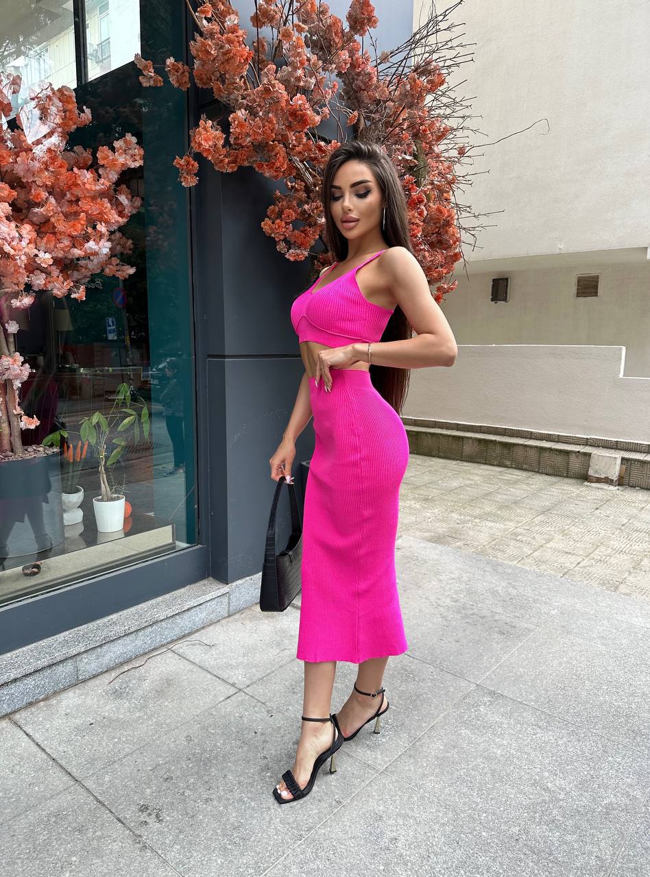 Woman in a bright pink dress standing outside a building with decorative plants.