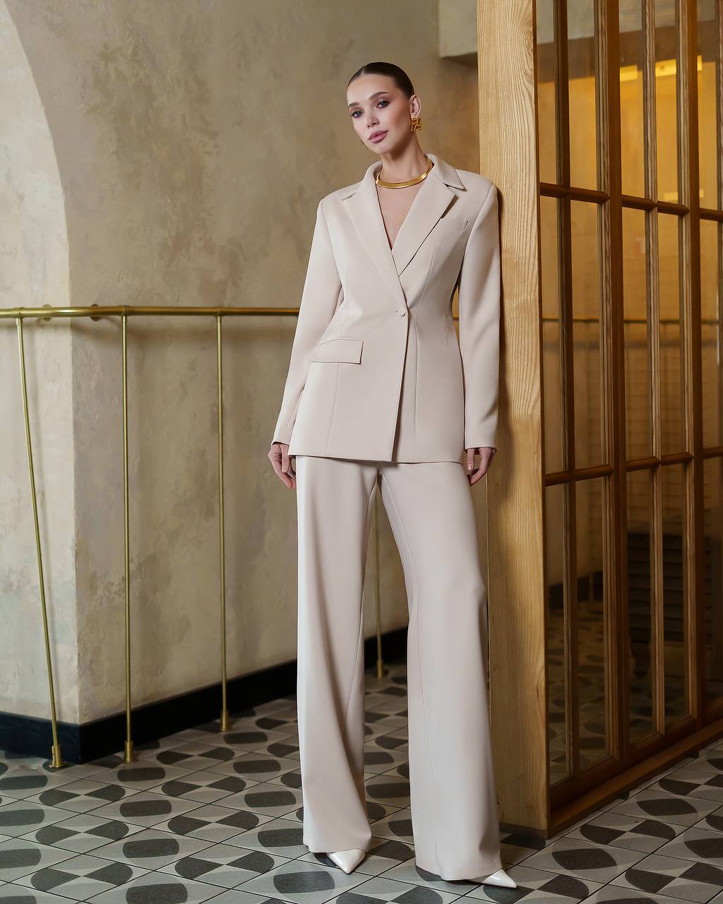 Woman in a beige suit standing in an elegant interior setting.