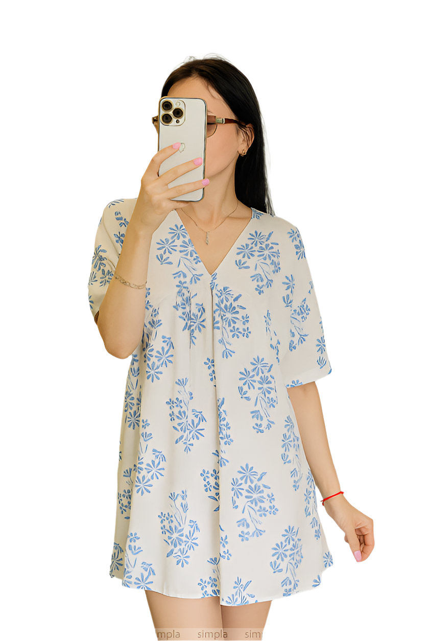 Woman wearing a floral dress taking a mirror selfie on a white background