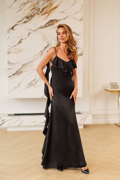Woman in a black evening gown standing in a stylish interior setting.