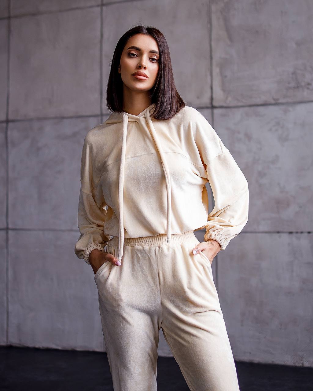 Woman wearing a beige outfit against a gray tiled wall