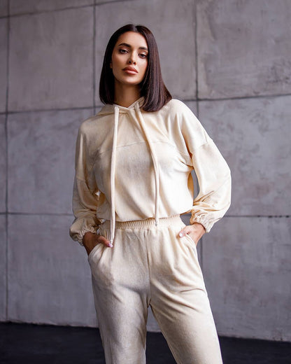 Woman wearing a beige outfit against a gray tiled wall
