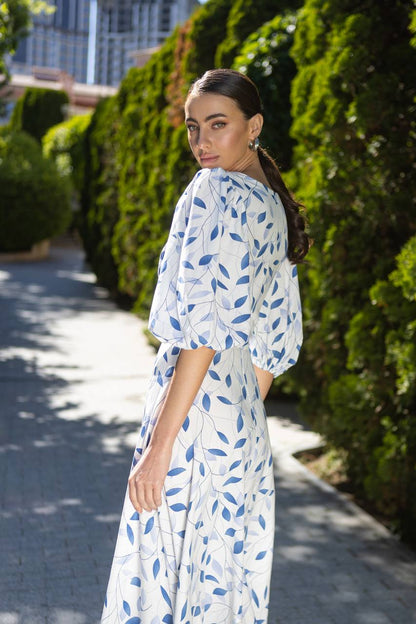 Woman in a white dress with blue leaf pattern walking outdoors.