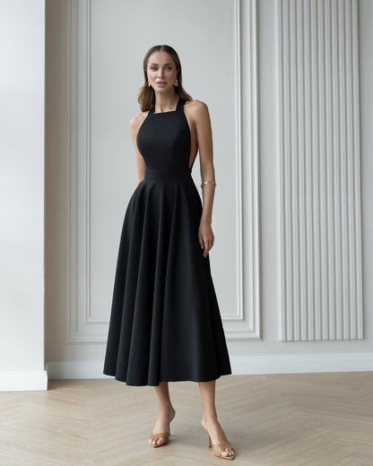 Woman wearing a black dress standing in a room with white walls and wooden floor.