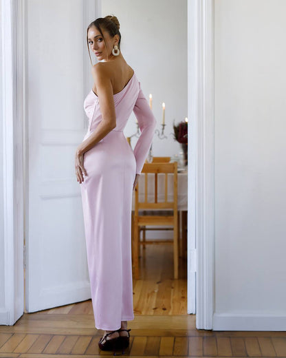 Woman in a pink dress standing in a room with wooden flooring and white walls.