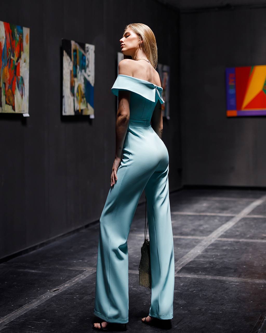 Woman in a light blue off-shoulder jumpsuit standing in an art gallery.