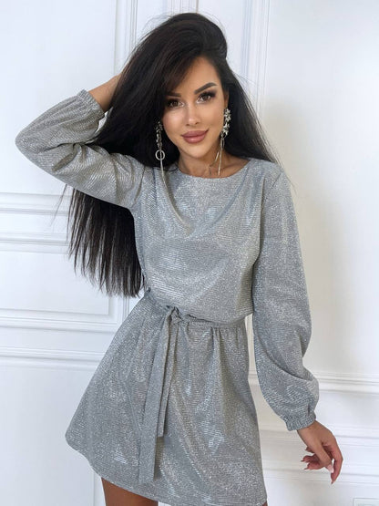 Woman wearing a gray patterned dress against a white wall