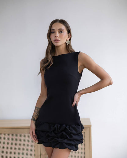Woman wearing a black dress with ruffled bottom half against a white background