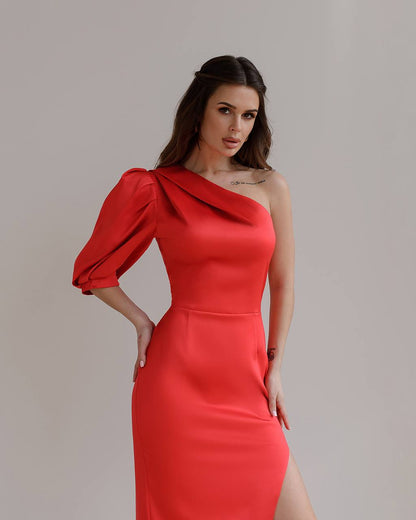 Woman wearing a red one-shoulder dress with puff sleeves against a plain background