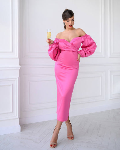 Woman in a pink off-shoulder dress holding a glass against a white wall.