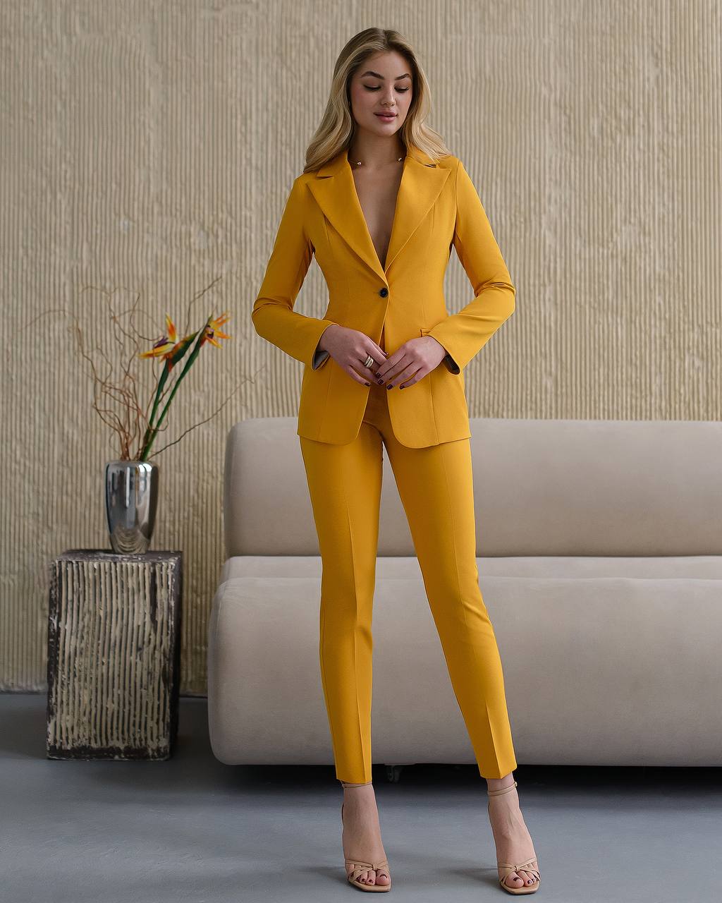 Woman in a yellow suit standing in a room with a couch and decorative plant.