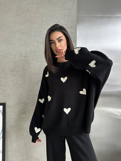 Woman wearing a black sweater with white heart patterns against a neutral background