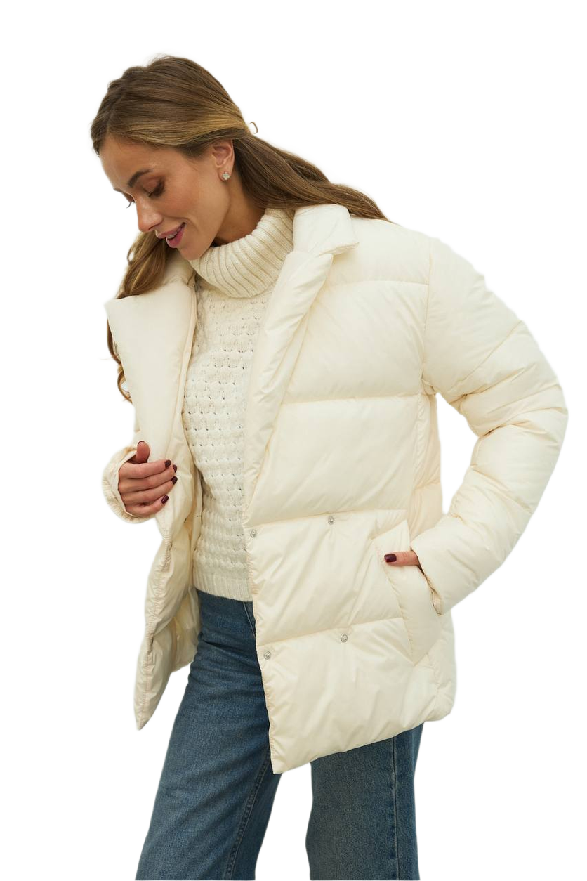 Woman wearing a cream puffer jacket over a knitted sweater on a white background